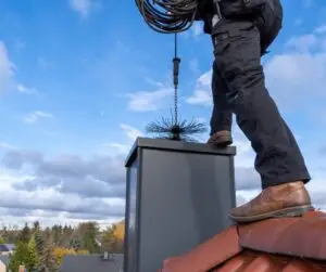 Man standing on roof with a chimney cleaning brush going down the chimney.