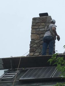 Man on roof with saftey straps around chimney for chimney repoint repair